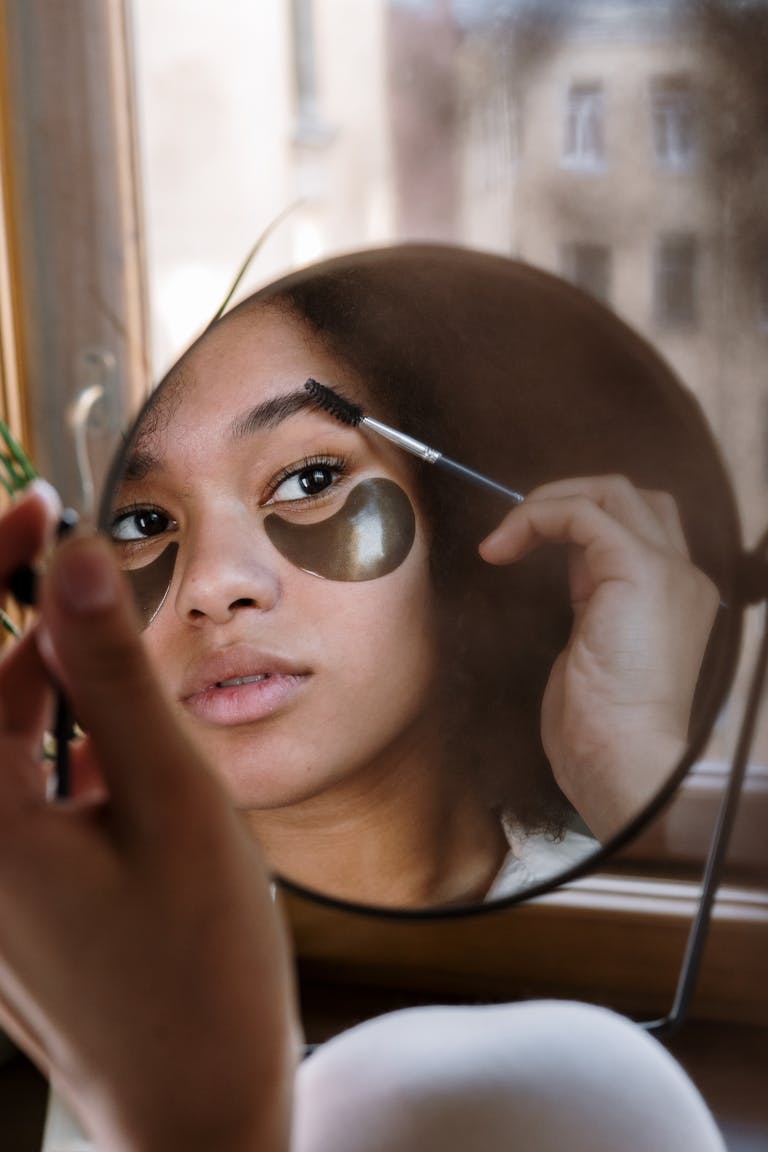 A reflective moment of a young woman applying makeup at home, captured in a mirror reflection.