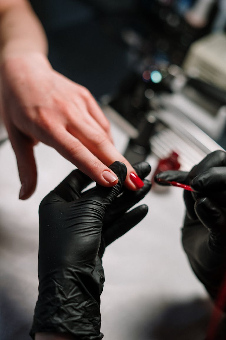 Close-up of a nail artist applying polish with precision using black gloves in a salon setting.